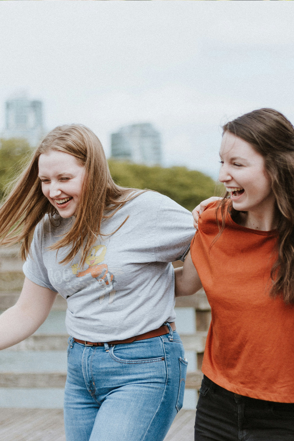 Zwei junge Frauen laufen lachend und Arm in Arm über eine Promenade