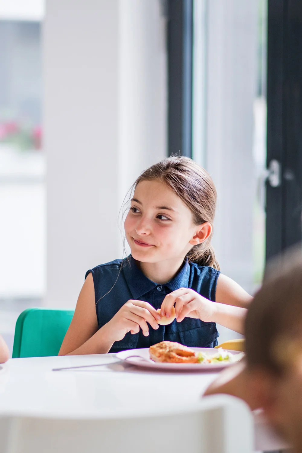 Lächelndes Mädchen sitzt beim Essen in der Kita-/Schulmensa