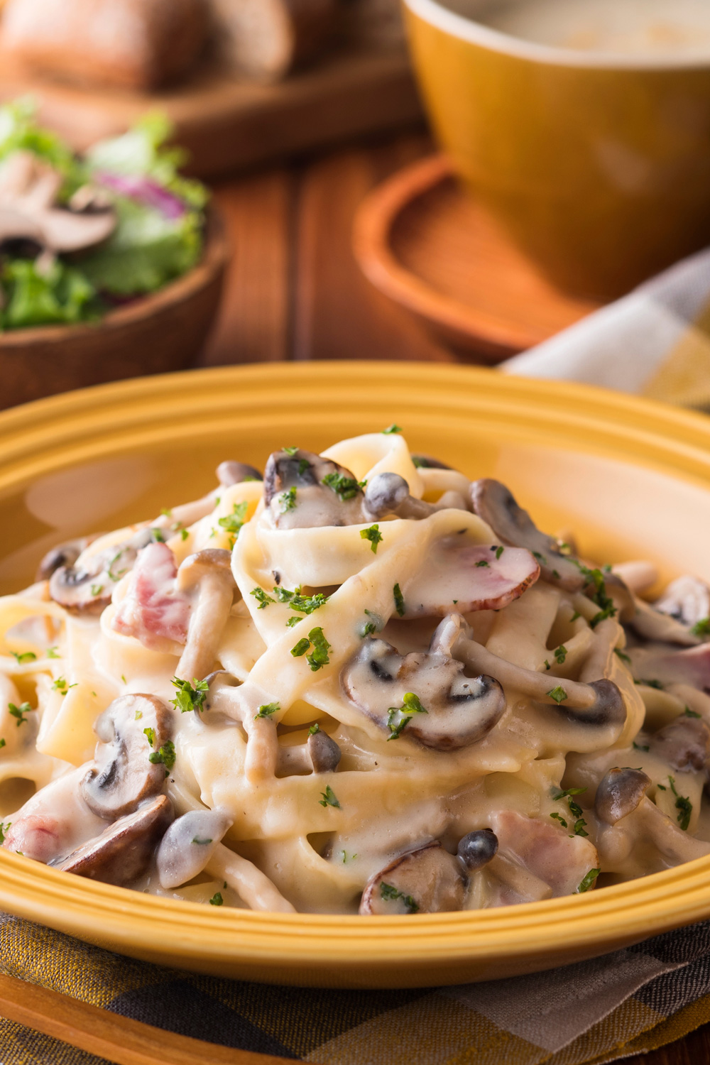 Teller mit cremiger Bandnudel-Pilz-Pfanne, im Hintergrund Salat und eine Tasse Suppe